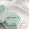  A rose gold diamond-textured stacking ring displayed inside a green velvet hexagonal ring box, with additional rings scattered beside it.